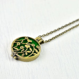Puede incluir: Un collar con un medallón verde y dorado con un diseño floral. El medallón está abierto y tiene un fondo de esmalte verde con un delicado patrón floral y pequeños corazones.