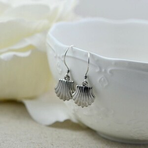 May include: Silver earrings with a seashell design. The earrings are hanging from a white bowl.