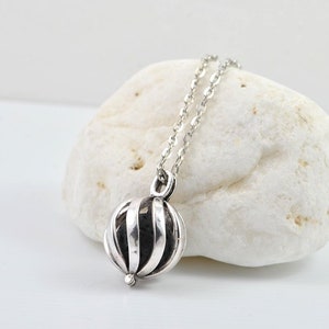 May include: A silver necklace with a round, cage-like pendant. The pendant has a textured, striped design.
