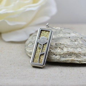 May include: A silver pendant necklace with a rectangular frame containing a gold glitter background and a silver silhouette of a rose.