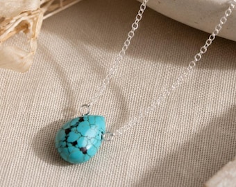 May include: A silver chain necklace featuring a single teardrop-shaped turquoise pendant with black matrix veining. The pendant is suspended from a delicate metallic link chain, showcasing a bright blue stone with natural dark mineral inclusions.