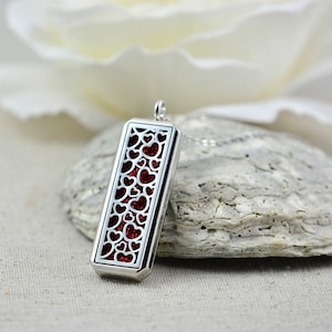 May include: Silver pendant necklace with a rectangular locket featuring a delicate heart design. The locket is open and reveals a red glitter interior.