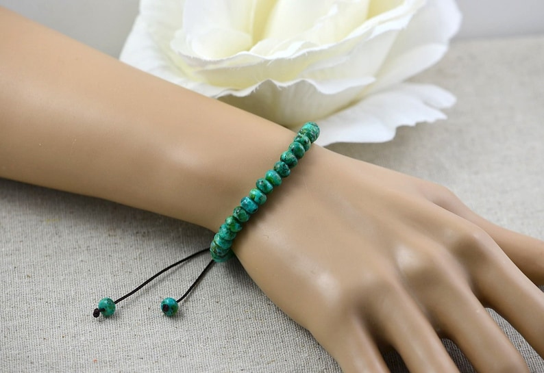 May include: A green turquoise beaded bracelet with a black cord and adjustable sliding knots.