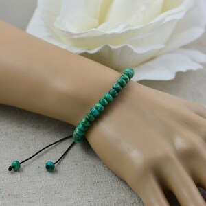 May include: A green turquoise beaded bracelet with a black cord and adjustable sliding knots.