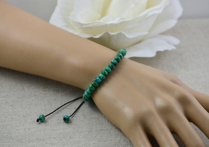 May include: A green turquoise beaded bracelet with a black cord and adjustable sliding knots.
