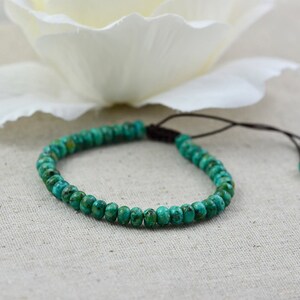 May include: A turquoise beaded bracelet with a brown cord closure. The bracelet is made of small, round beads and is tied with a simple knot.