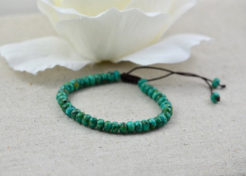May include: A turquoise beaded bracelet with a brown cord closure. The bracelet is made of small, round beads and is tied with a simple knot.