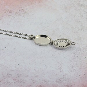 May include: A silver necklace with a round pendant that opens to reveal a decorative design. The pendant is attached to a delicate silver chain.