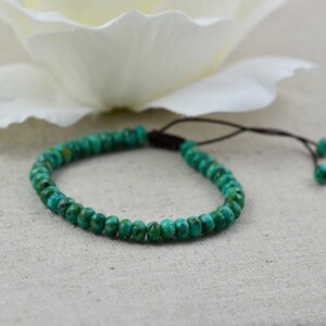 May include: A turquoise beaded bracelet with a brown cord closure. The bracelet is made of small, round beads and is adjustable.