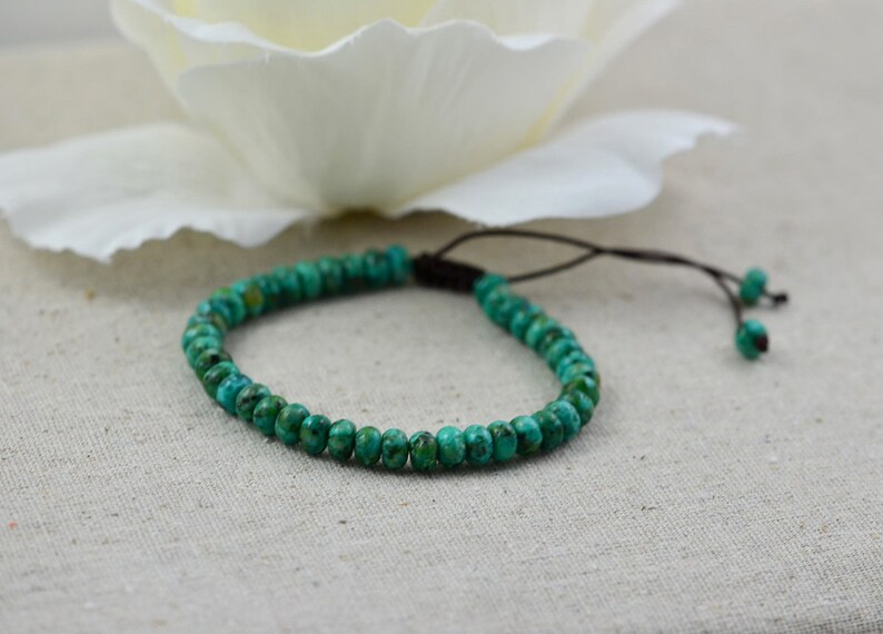 May include: A turquoise beaded bracelet with a brown cord closure. The bracelet is made of small, round beads and is adjustable.