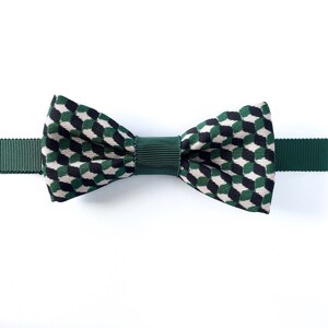 May include: A green bow tie with a black and white geometric pattern. The bow tie is made of a thick, textured fabric.