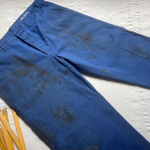 Puede incluir: Un par de pantalones de trabajo azules con manchas oscuras y la palabra "PECORON" en la cintura.