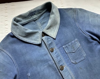 May include: A blue denim jacket with a large collar and a single chest pocket. The jacket has a faded look and is made of a thick, durable fabric.