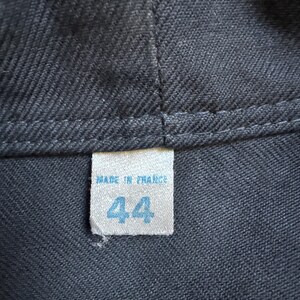 May include: Close-up of a dark gray fabric with a stitched seam. A small, rectangular tag is sewn onto the fabric, displaying the text "MADE IN FRANCE" above the number "44" in blue.