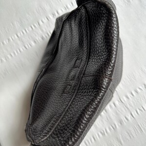 May include: A dark brown leather handbag with a textured surface. The bag has a knotted handle and a structured design. The image shows the top and side of the bag, highlighting the details of the leather.