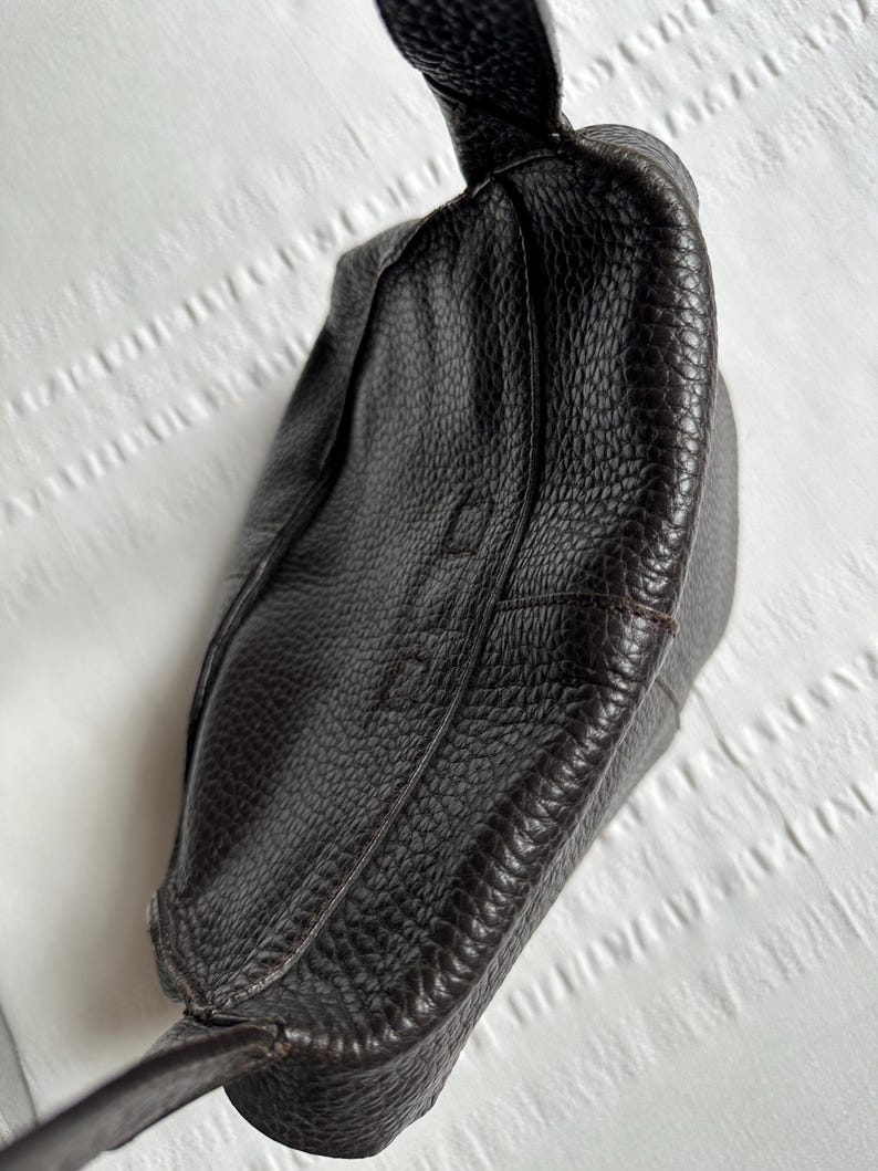 May include: A dark brown leather handbag with a textured surface. The bag has a knotted handle and a structured design. The image shows the top and side of the bag, highlighting the details of the leather.