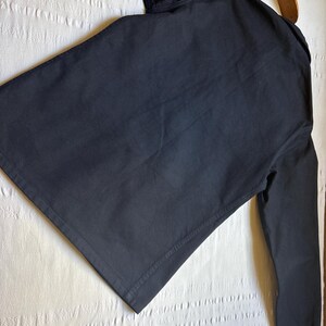 May include: A black long-sleeved shirt with a collar, hanging on a wooden hanger. The shirt is made of a solid, dark fabric. The sleeves are long and the cuffs are buttoned.