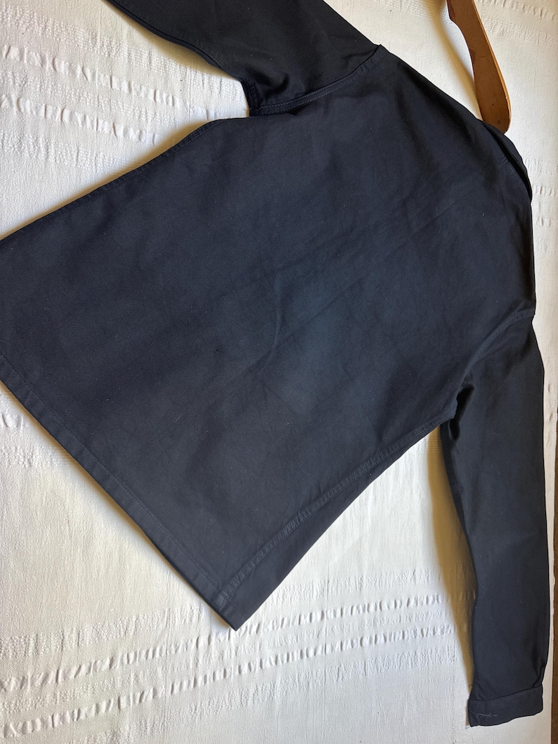 May include: A black long-sleeved shirt with a collar, hanging on a wooden hanger. The shirt is made of a solid, dark fabric. The sleeves are long and the cuffs are buttoned.