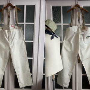 May include: White cotton overalls with suspenders and a button closure. The overalls have a relaxed fit and are made of a lightweight fabric.