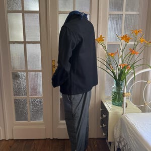 May include: A black jacket and gray pants are worn by a person. The jacket has a collar and the pants have a drawstring at the ankle. The person is standing in front of a white door with glass panes. The floor is made of wood.