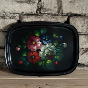 May include: Black rectangular serving tray with a hand-painted floral design. The flowers are in shades of red, pink, white, and blue, with green leaves. The tray is made of a dark material and has a glossy finish.