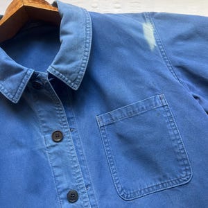 May include: A blue denim work shirt with a single chest pocket and button closure. The shirt has a collar and long sleeves.