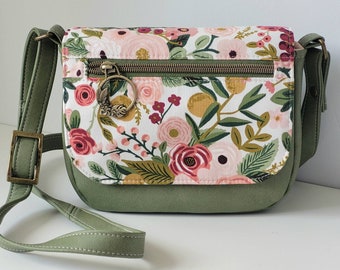 May include: A green crossbody bag with a floral print fabric flap and a gold zipper pull. The bag has a long adjustable strap.