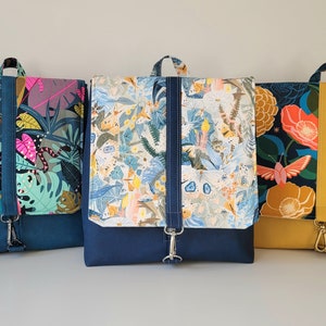 May include: Three different fabric backpacks with colorful floral and leaf patterns. The backpacks are all navy blue with a flap closure and a single strap.
