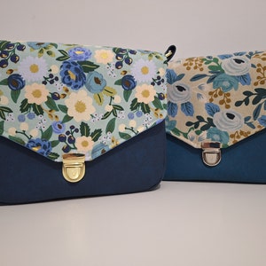 Könnte beinhalten: Zwei blaue und marineblaue Umhängetaschen mit Blumenmustern. Die Tasche links hat einen hellblauen Hintergrund mit weißen und blauen Blumen. Die Tasche rechts hat einen beigefarbenen Hintergrund mit weißen und blauen Blumen.