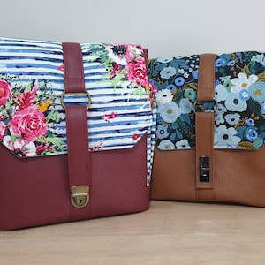 Pode incluir: Duas bolsas de tecido com padrões florais. A bolsa à esquerda tem um tecido listrado azul e branco com flores rosa e brancas. A bolsa à direita tem um tecido preto com flores azuis e brancas. Ambas as bolsas têm alças de couro castanho e uma aba de couro castanho.