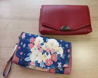 Puede incluir: Dos clutches, una roja y otra con estampado floral. La clutch floral tiene una solapa rosa y una tela azul con flores blancas y rosas. La clutch roja tiene un cierre plateado.