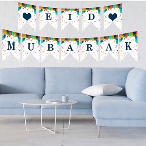 May include: A white banner with colorful confetti and the words "Eid Mubarak" in blue letters. The banner is strung up on a white wall above a light blue sectional sofa.
