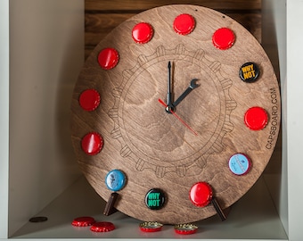May include: A wooden clock with a gear design and bottle caps for numbers. The clock hands are black and red. The clock is on a white shelf with bottle caps scattered around it. The clock face says "WHY NOT" and "CAPS&BOARD.COM".