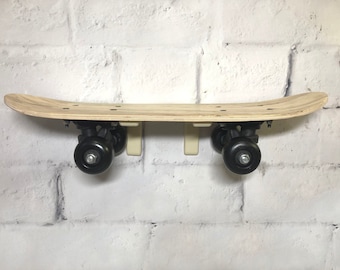 May include: A wooden skateboard with black wheels is mounted on a white brick wall using two white plastic hooks.