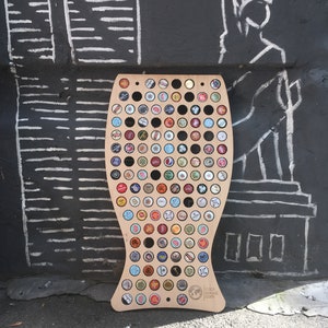 Peut inclure: Un porte-capsule de bouteille en bois en forme de poisson avec une finition en bois brun. Le porte-capsule est rempli de capsules de bouteille de différentes couleurs et motifs. Le texte "cape board room.com" est imprimé au bas du porte-capsule.