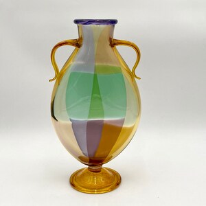 May include: A colorful glass vase with two handles and a round base. The vase is decorated with stripes of green, purple, and brown.