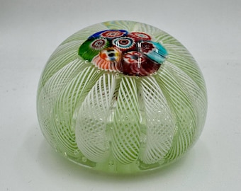 May include: A round, green glass paperweight with a swirl design and a cluster of colorful millefiori flowers on top. The paperweight has a clear, bubble-like texture and is approximately 3 inches in diameter.