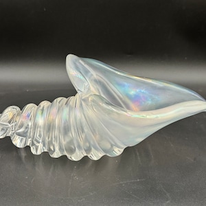 May include: A white iridescent glass seashell shaped bowl. The bowl is made of glass and has a swirling pattern.