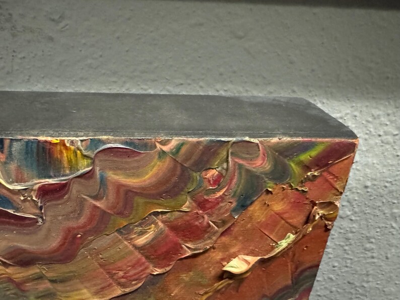 Puede incluir: Primer plano de una esquina de una pintura con pinceladas gruesas y texturizadas. Los colores incluyen tonos de rojo, naranja, amarillo, azul y verde. El borde superior es gris oscuro y el fondo es gris claro.