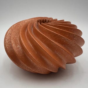 Puede incluir: Un jarrón de cerámica de color terracota con un diseño en espiral giratorio. El jarrón tiene una superficie texturizada y moteada.