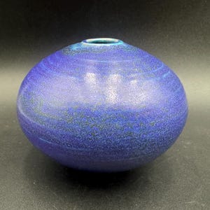 May include: A small, round, blue ceramic vase with a swirling pattern. The vase has a smooth, glossy finish.