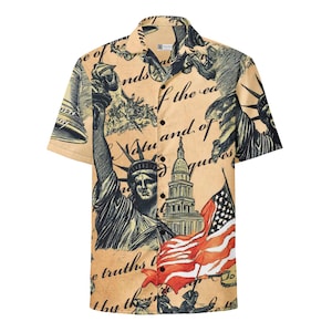 May include: Short-sleeved button-down shirt with a beige background and a patriotic design. The shirt features illustrations of the Statue of Liberty, the American flag, and historical documents. The design is in shades of black, red, and beige.