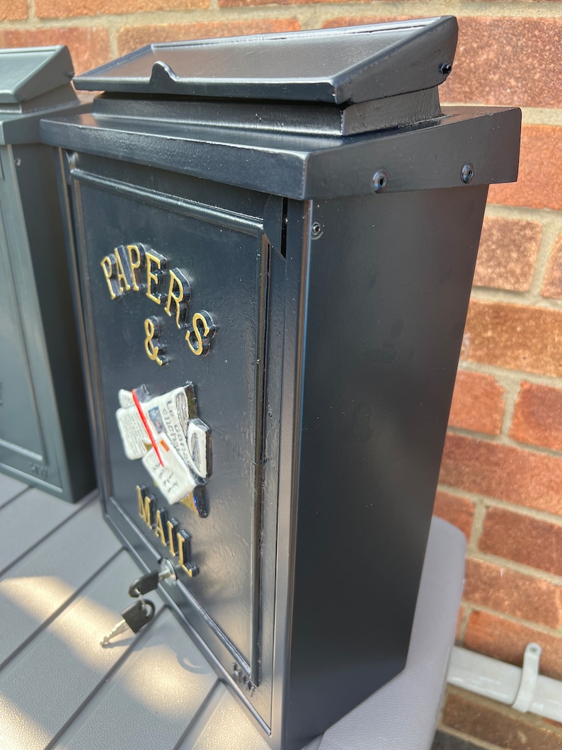 May include: Black metal mailbox with a gold inscription that reads "Papers & Mail". The mailbox has a slot for mail and a keyhole.