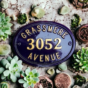 May include: A purple and gold oval-shaped house number sign with the text "Grassmere 3052 Avenue".
