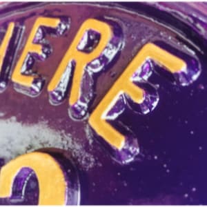 May include: Close-up of a purple metal surface with the word "HERE" in yellow lettering.