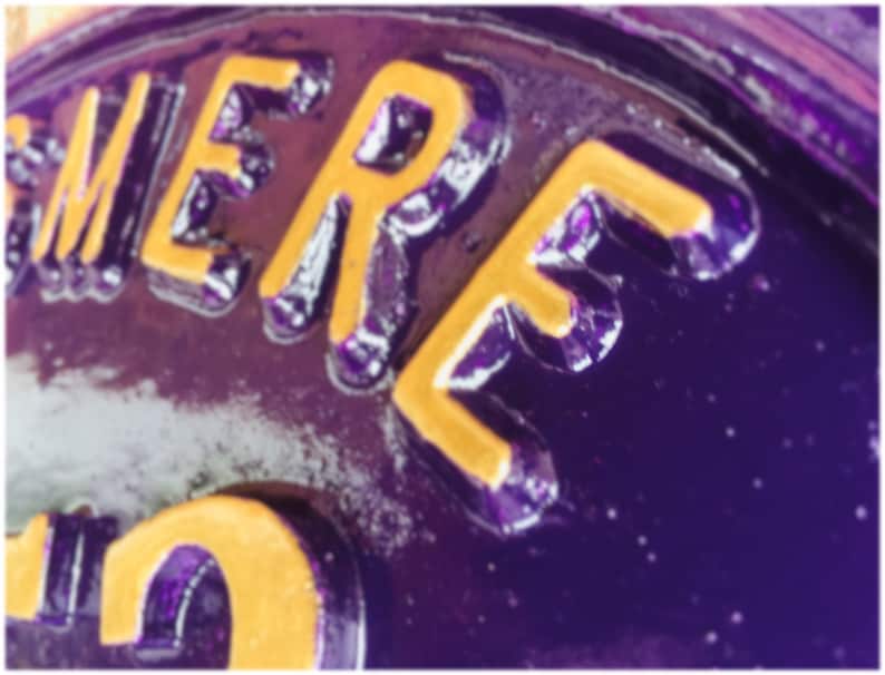 May include: Close-up of a purple metal surface with the word "HERE" in yellow lettering.
