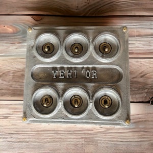 May include: A silver metal switch plate with six round toggle switches and the text "YEHI 'OR" embossed on the front. The switches have brass toggles.