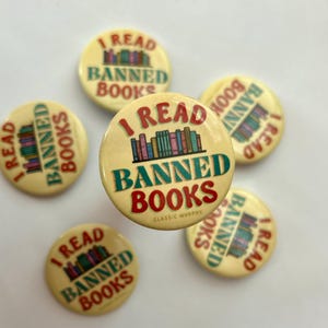 Può includere: Cinque bottoni rotondi gialli con il testo "I Read Banned Books" in lettere rosse, verdi e blu. I bottoni presentano una pila di libri colorati e il testo "Classic Murphy".
