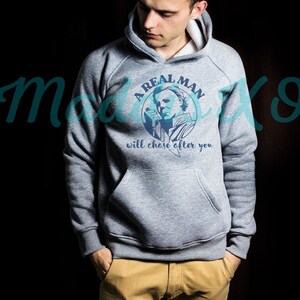 May include: A gray hooded sweatshirt with a graphic print of a man with a knife and the text "A Real Man Will Chase After You".
