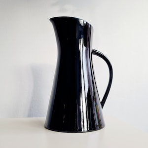 Puede incluir: Una jarra de cerámica negra con una base ancha y un pico estrecho. La jarra tiene un acabado brillante y un diseño simple y elegante.